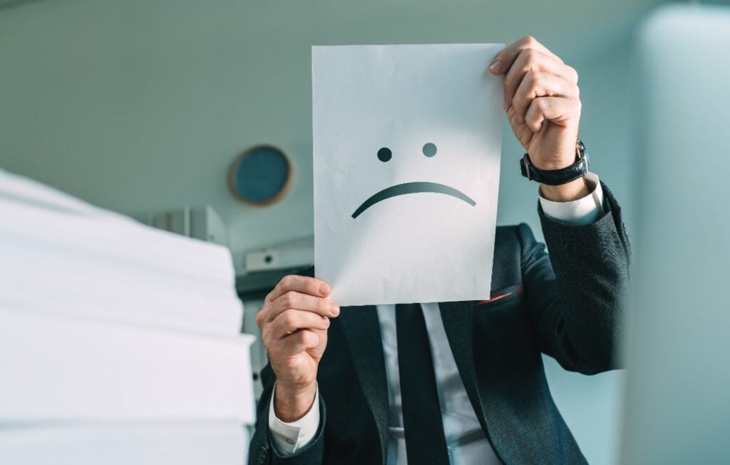 businessman holding paper with frowning emoticon in office interior