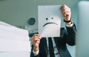 businessman holding paper with frowning emoticon in office interior