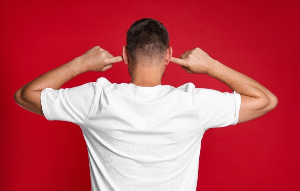 Man covering his ears with fingers on red background, back view
