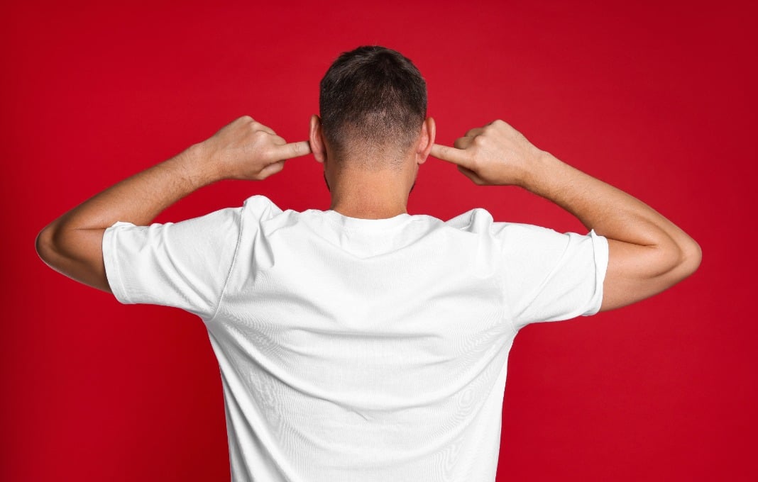 Man covering his ears with fingers on red background, back view