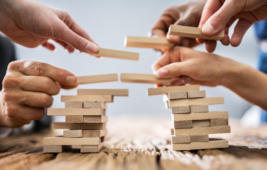 Various hands building a bridge out of wooden blocks
