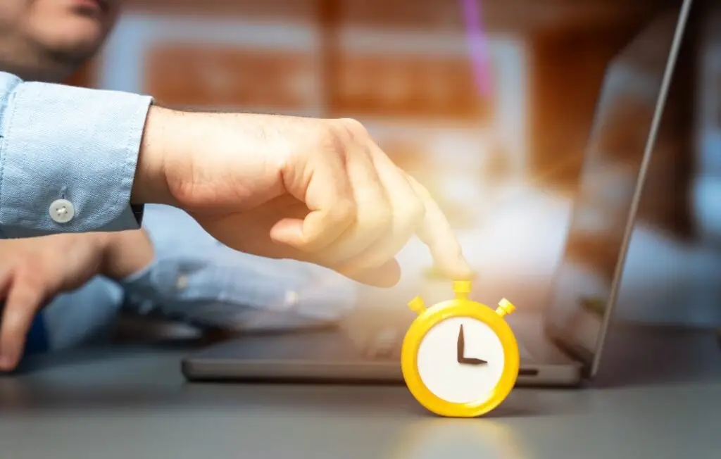 Businessman presses a stopwatch and an alarm clock while sitting in an office at a laptop.
