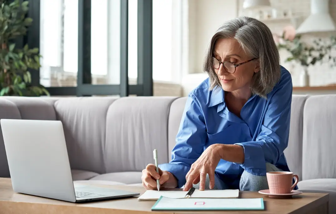 woman remote working from home distance office on laptop taking notes.